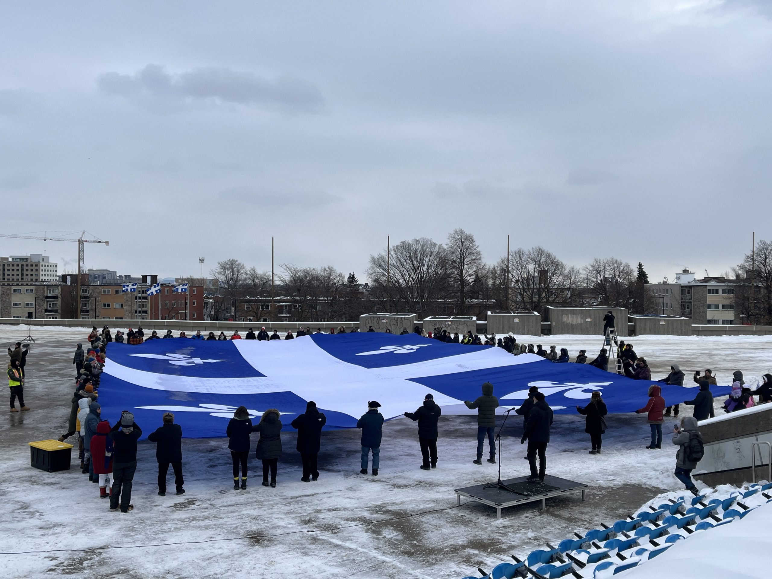 Des participants déploient un immense drapeau du Québec lors du Jour du drapeau. © Salomé Dano