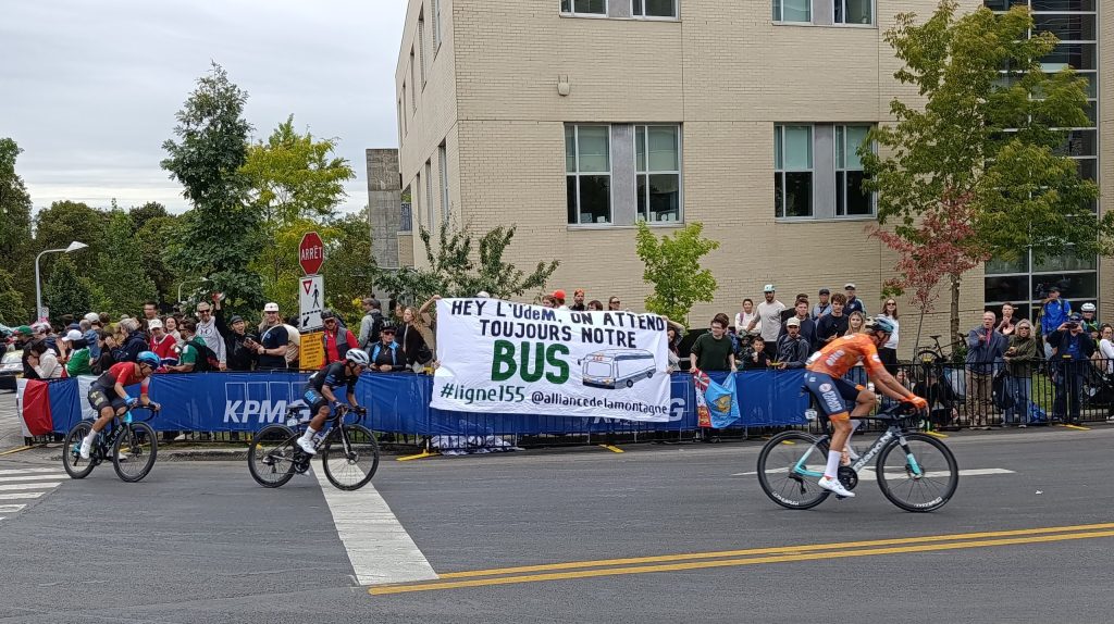 Les étudiants de l'Alliance de la Montagne pour l'Écologie brandissent leur banderole qui appelle pour une ligne de bus sur la montagne lors de la dernière journée des Championnats du monde sur route de 2026. Crédit : Leane Fautrat